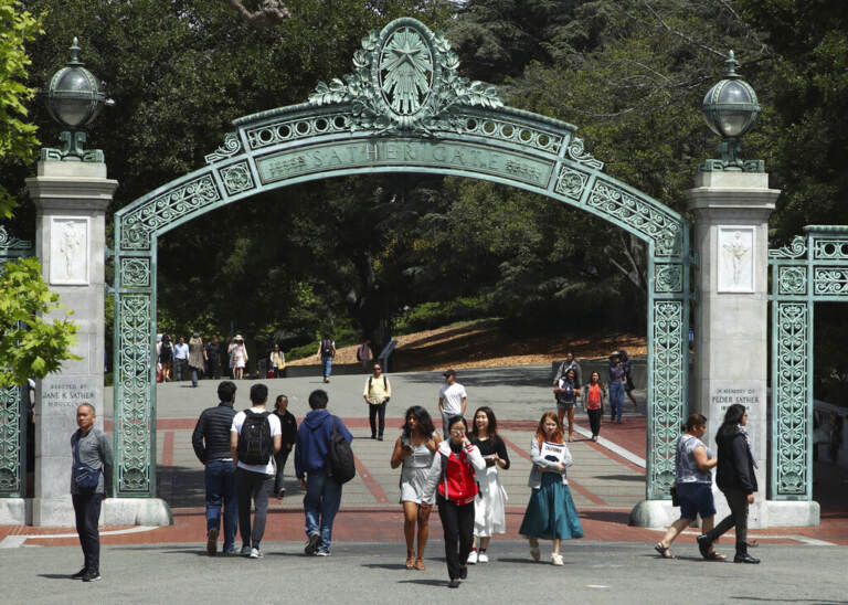 Students walk through a green arch on a college campus.