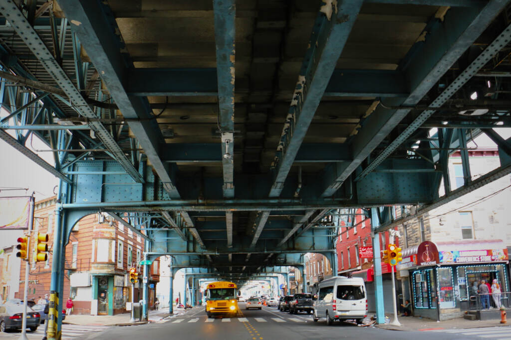 Cars drive on the street underneath the elevated train tracks.