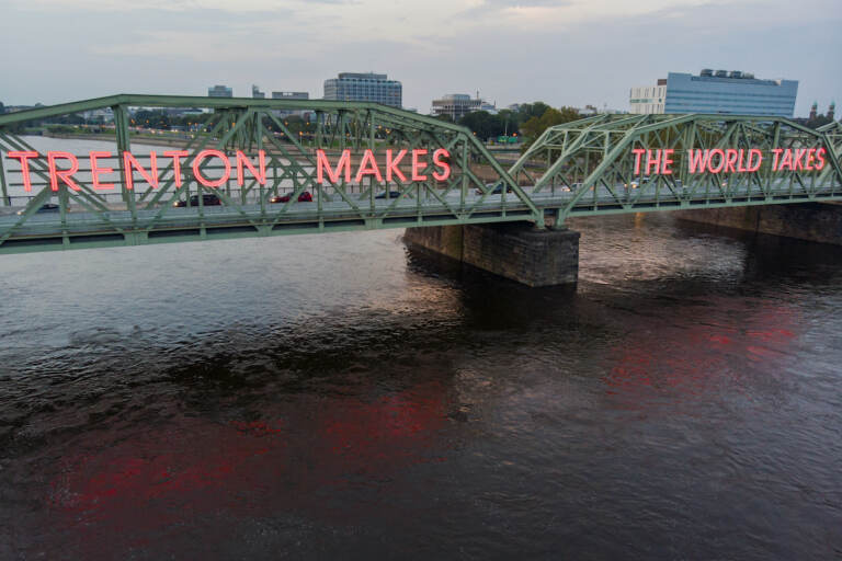 A bridge over a river with large neon lights spelling out 'Trenton Makes the World Takes''