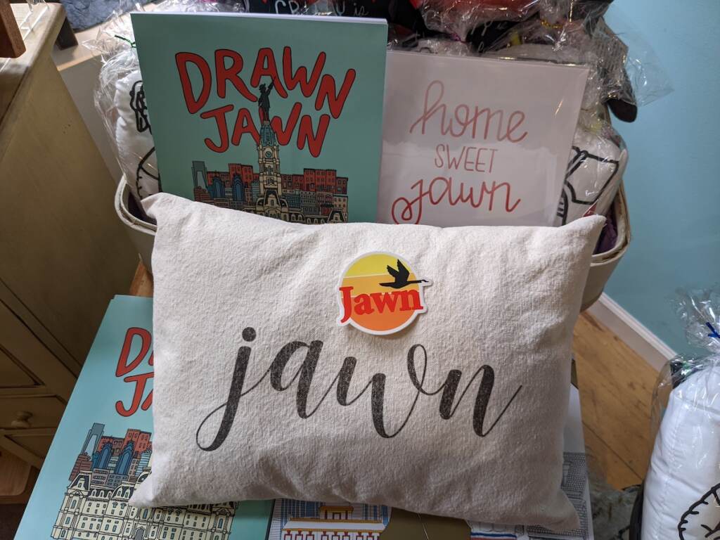 PXL_20221012_203949926 Pictured items include a jawn pillow from The Pillow Works, the Drawn Jawn coloring book by Katie Otte, a jawn sticker from South Fellini and a print that says