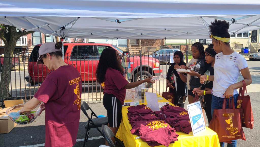 People approach a table with T-shirts in an outdoor tent.