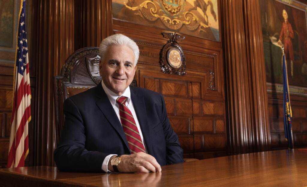 chief-justice-max-baer-death Chief Justice Max Baer sits at a wood table with the U.S. flag in the background.