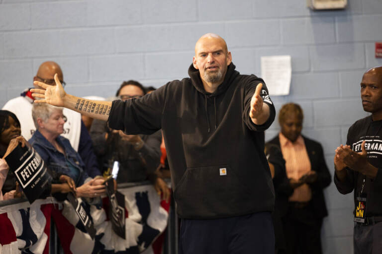 John Fetterman gestures with his arms while speaking as people look on.