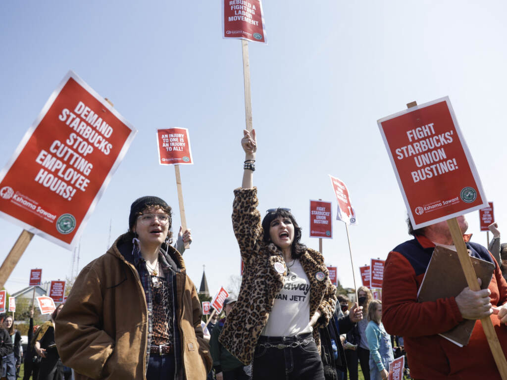 Marchers raise picket signs during a “Fight Starbucks’ Union Busting” rally held in Seattle in April. People hold up red picket signs.