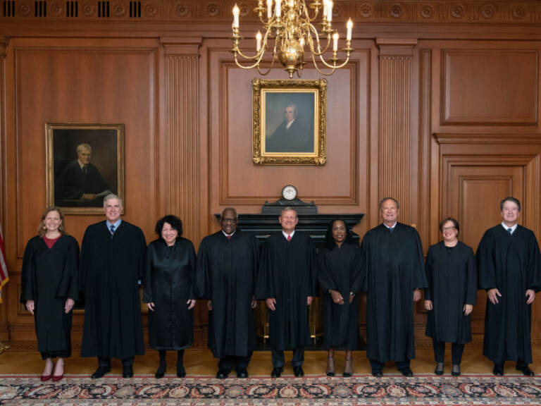 The U.S. Supreme Court Justice stand facing the camera in their court attire.