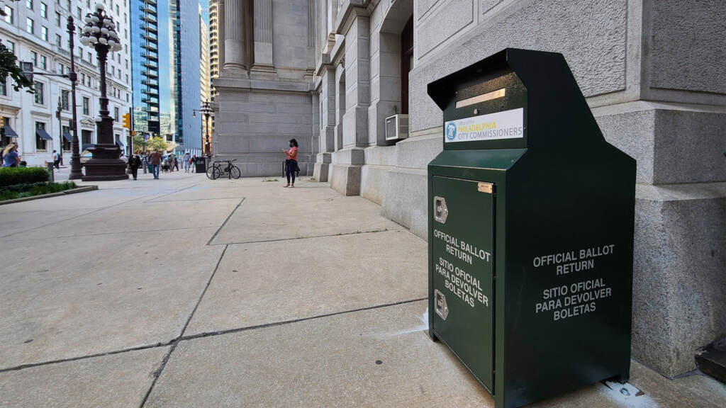 An up close photo of a ballot drop box stationed next to a building on a sidewalk.