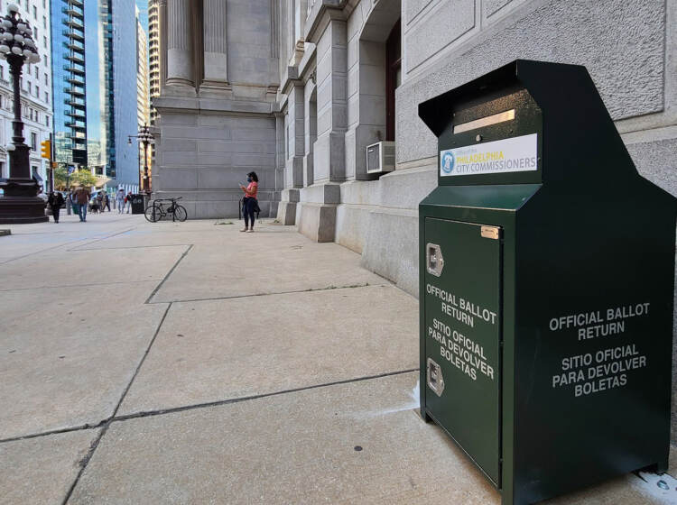 An up close photo of a ballot drop box stationed next to a building on a sidewalk.
