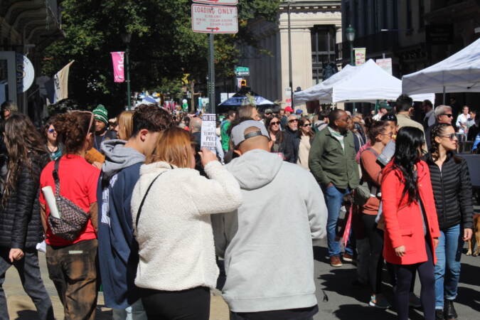 A crowd of people walks down a street lined with vendors' tents.