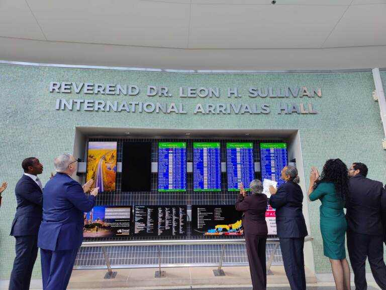 Mayor Jim Kenney (in blue) and Mable Ellis Welborn (in maroon), board chair of the Leon H. Sullivan Charitable Trust, unveil the new name of the international arrivals hall at the Philadelphia airport. (Peter Crimmins/WHYY)