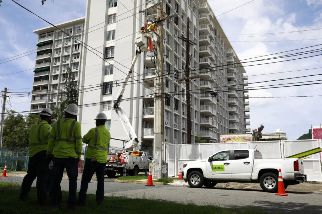 Hurricane Fiona Hits Puerto Rico, Knocking Out Power Across The Island Workers repair an electrical wire in front of a tall building.