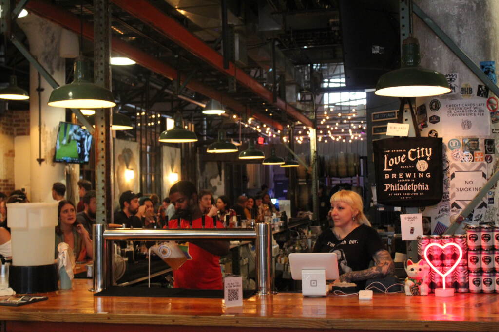 queertoberfest-1 People gather around a bar. A sign reads Love City Brewing.