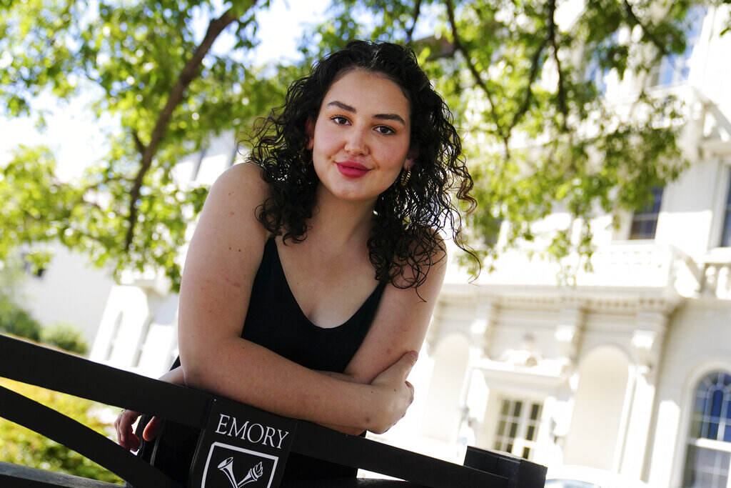 Helen Khuri A person poses for a photo, leaning up against a fence. A tree is visible in the background.