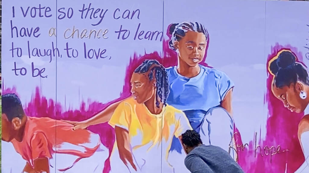 An artist paints a mural that is almost done, showing two people smiling.