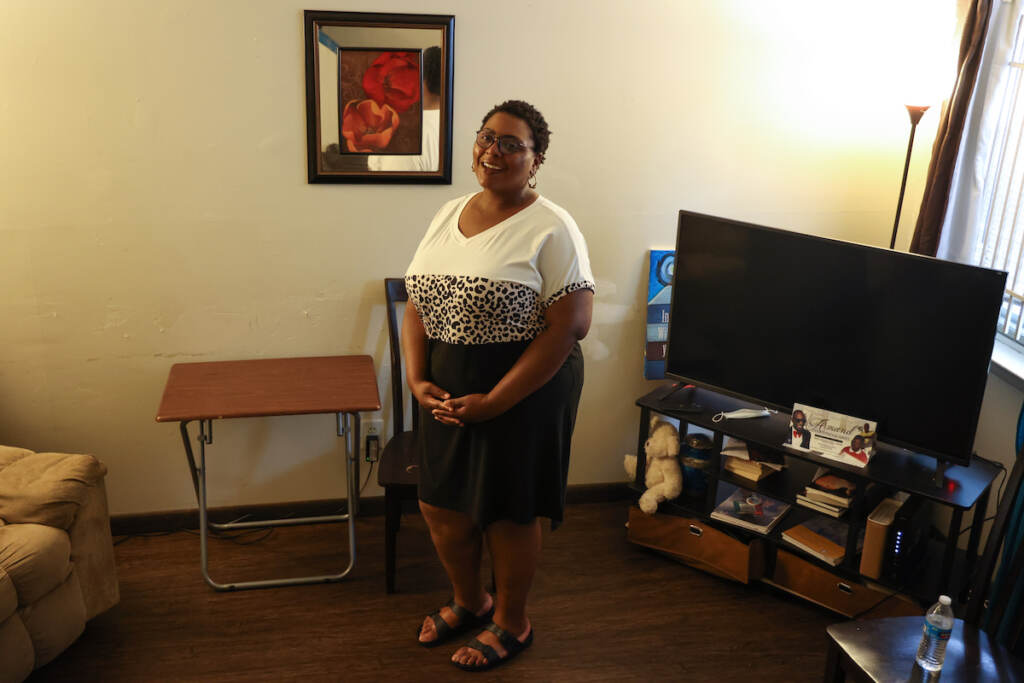 A woman stands, smiling, in the center of her living room.