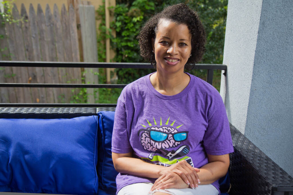 A woman sits on a porch seat, looking towards the camera.