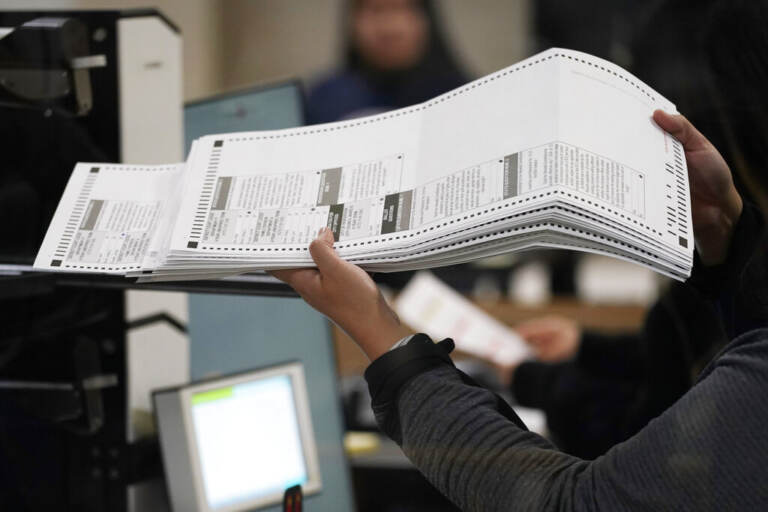 A person holds ballots in their hand as they feed them into a machine.