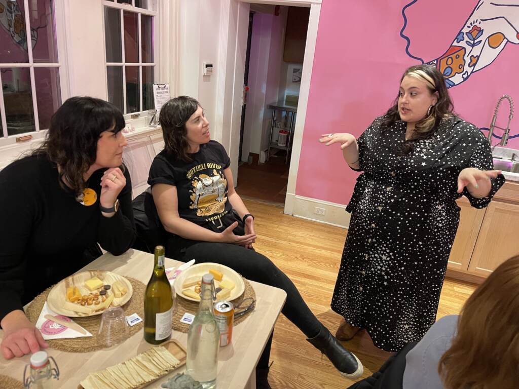 One person stands up and is talking, while two other people are seated at a table.