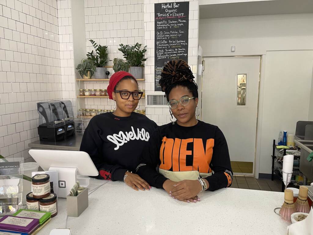 Dope_Botanicals_horiz (1) Two people stand at the counter of a store. Plants are visible in the background.