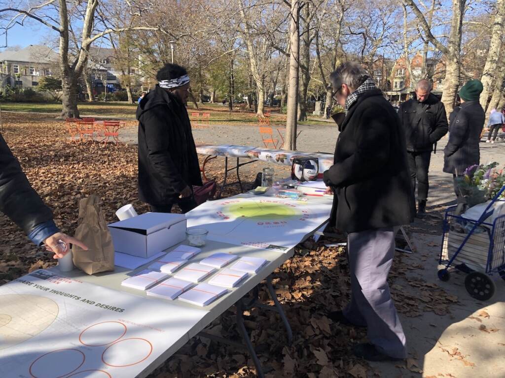 clark-park-1-11-19-22 People gather around a table in a park.