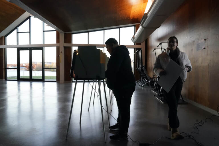 A voter walks to cast their ballot as another fills his out at the Eleanor Boathouse polling place on the Southside of Chicago, Tuesday, Nov. 8, 2022. (AP Photo/Charles Rex Arbogast)