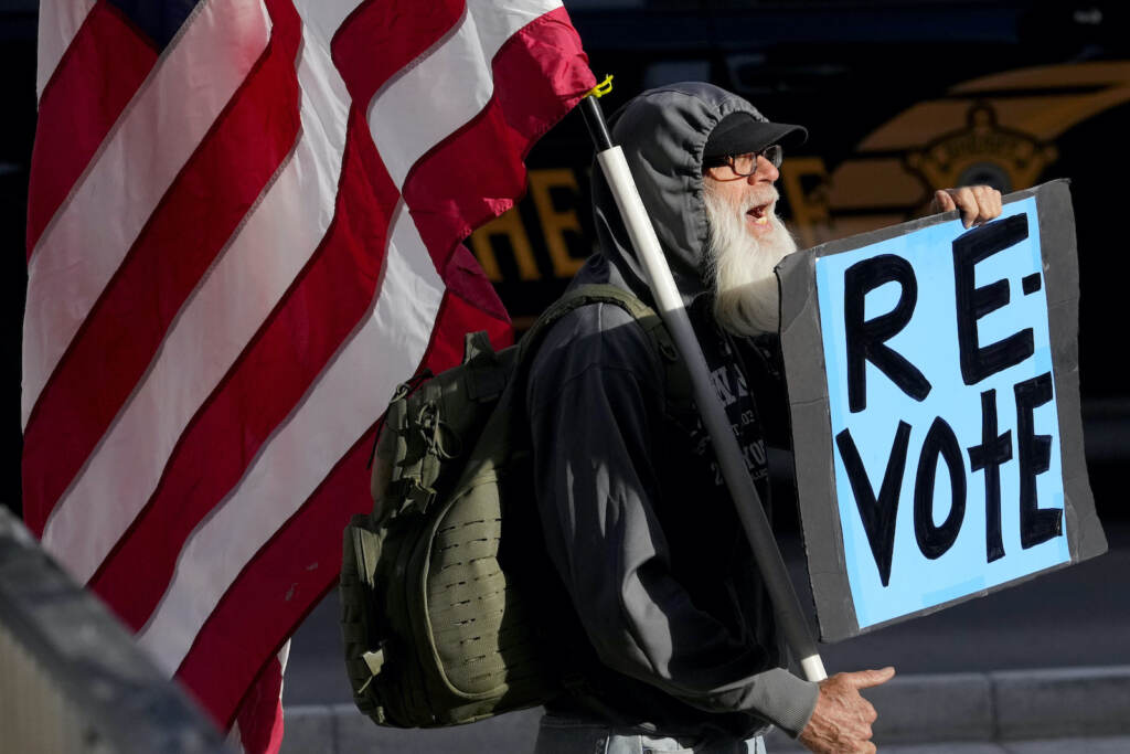 A man protests outside the Maricopa County Board of Supervisors auditorium prior to the board's general election canvass meeting, Nov. 28, 2022, in Phoenix.