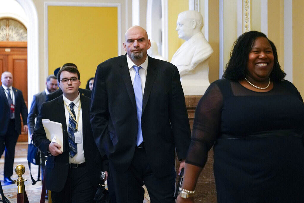 John Fetterman Fetterman walks along with other people down a hallway.