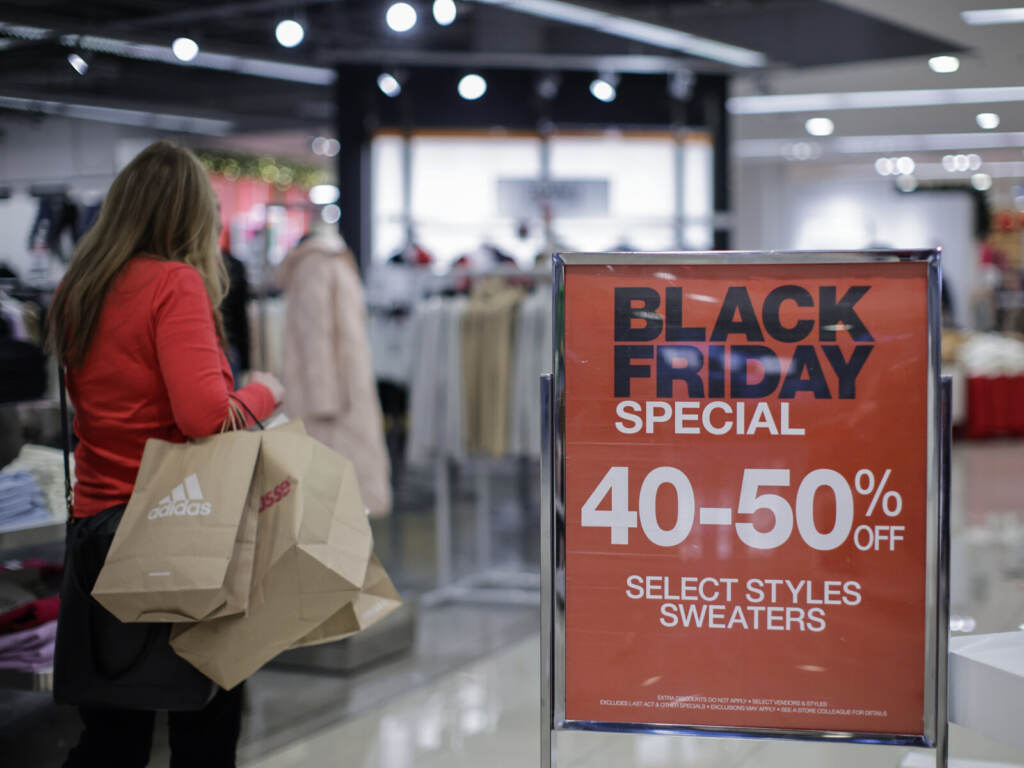 Shoppers Flock To Stores For Black Friday Deals A person with shopping bags walks by a sign advertising Black Friday sales.