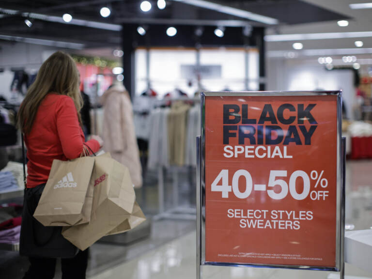 A person with shopping bags walks by a sign advertising Black Friday sales.