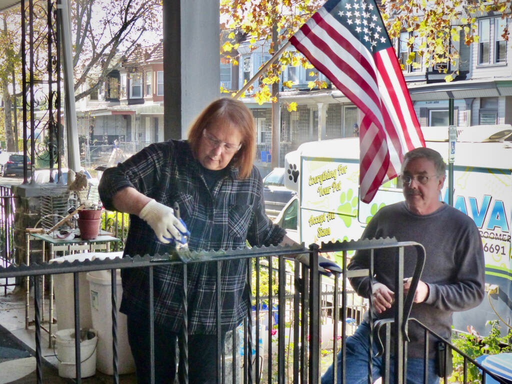 habitat-humanity-philadelphia-1 People paint the railing on a porch, with the U.S. flag flying in the background.