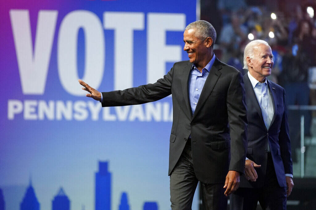 Obama waves as Joe Biden looks upward and smiles. Behind them is a sign that reads Vote Pennsylvania.