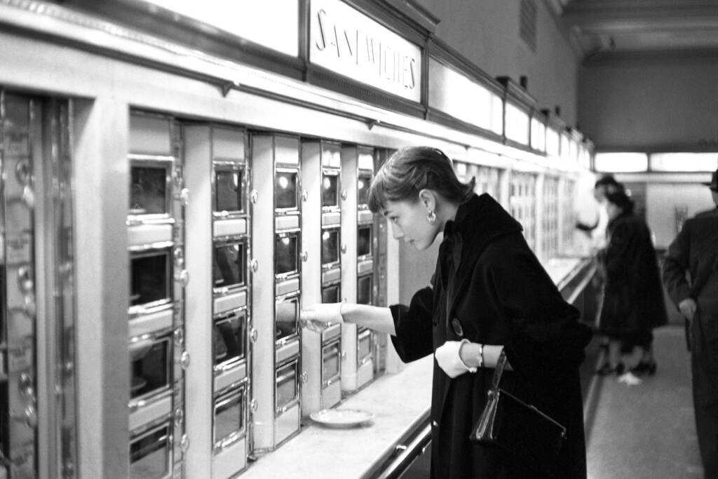 Audrey Hepburn A black-and-white photo of Audrey Hepburn looking at an automat.