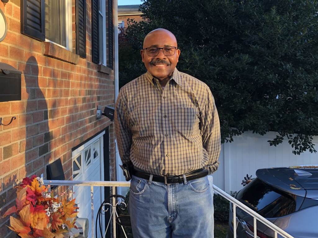A man smiles next to his house.