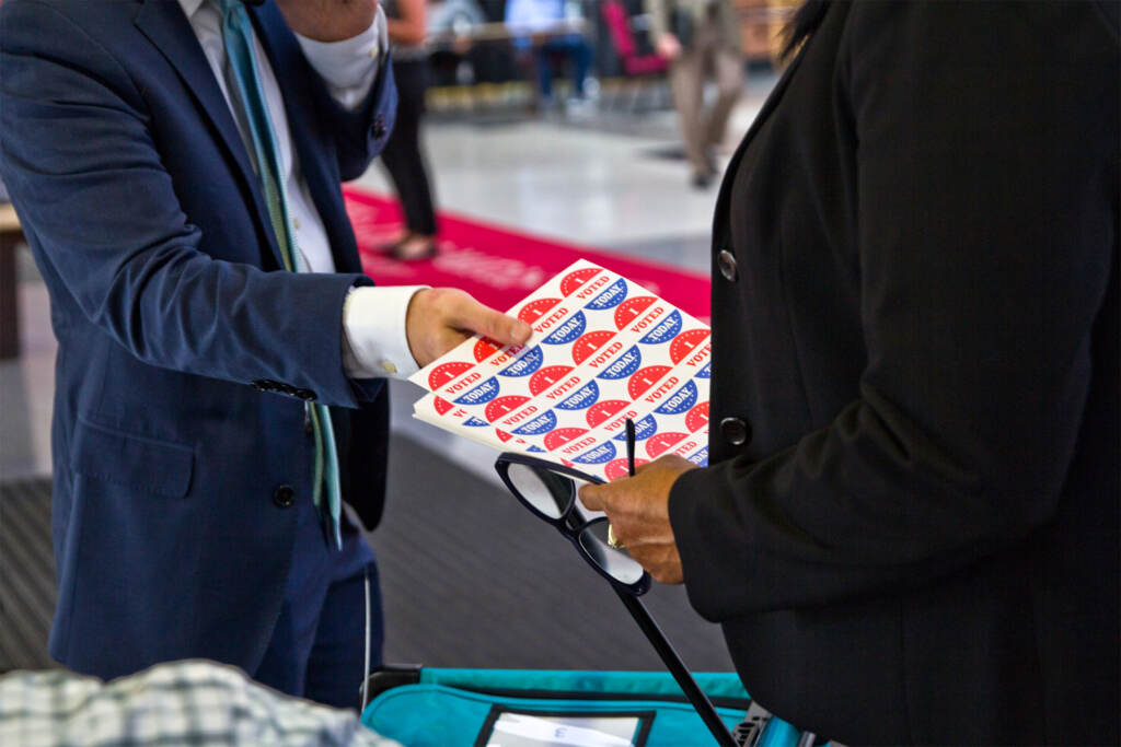 A person gives another person a sheet of I Voted stickers.