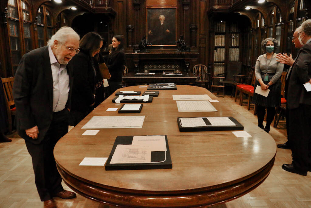 People walk around a table where papers are displayed.