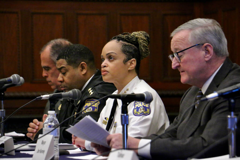 A row of people sit at a table with microphones in front of them.