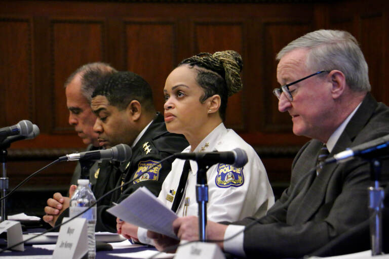 A row of people sit at a table with microphones in front of them.
