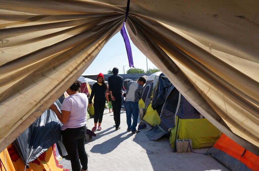 Mexico US Border People walk around, as seen through the parted curtains of a tent.