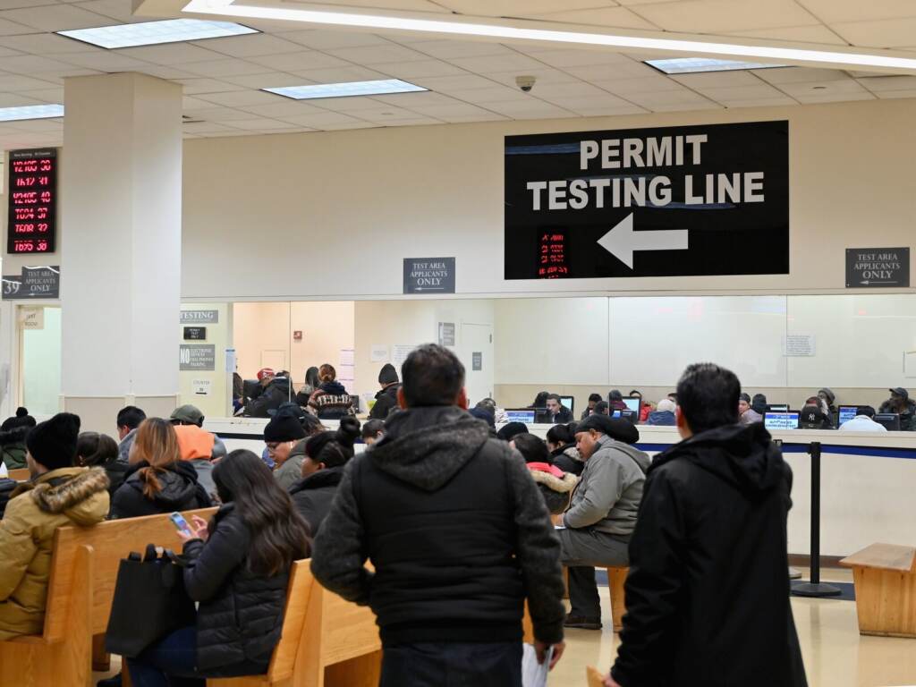 People wait in a large room. A sign reads 