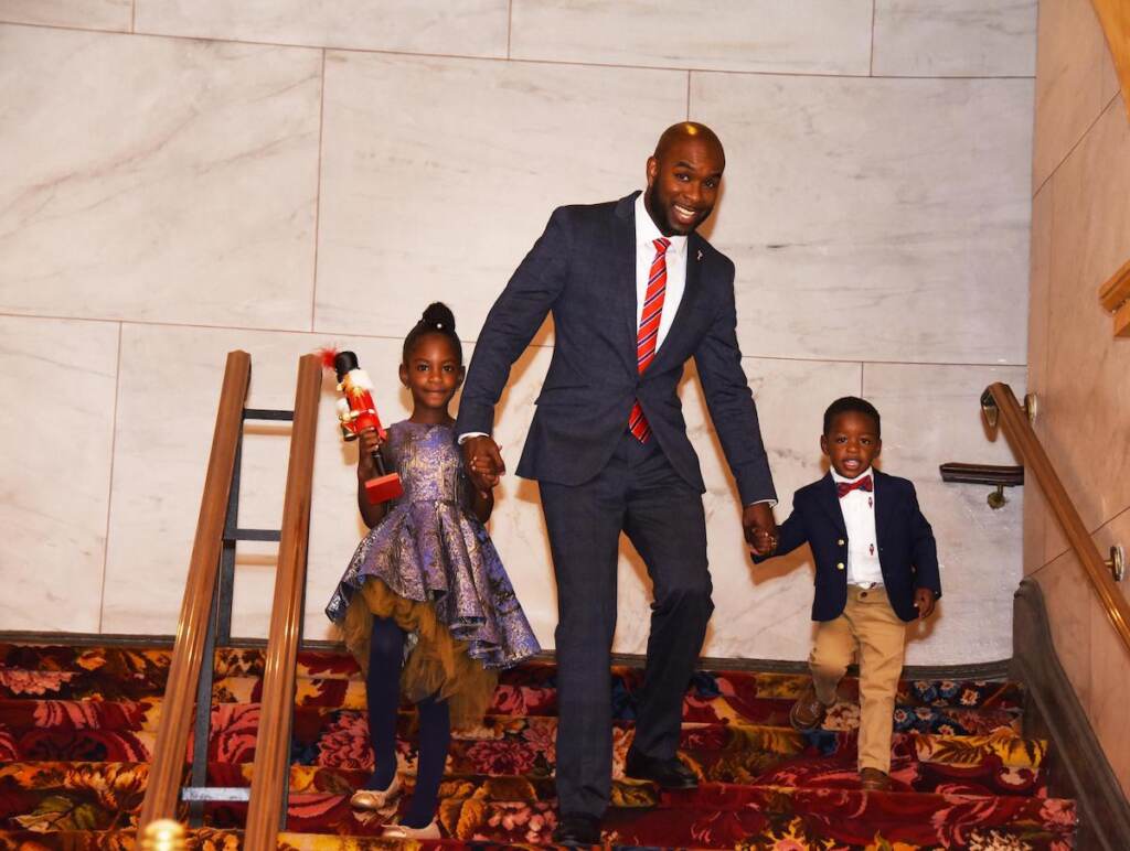 A man holds hands with his two children as they walk down the steps.