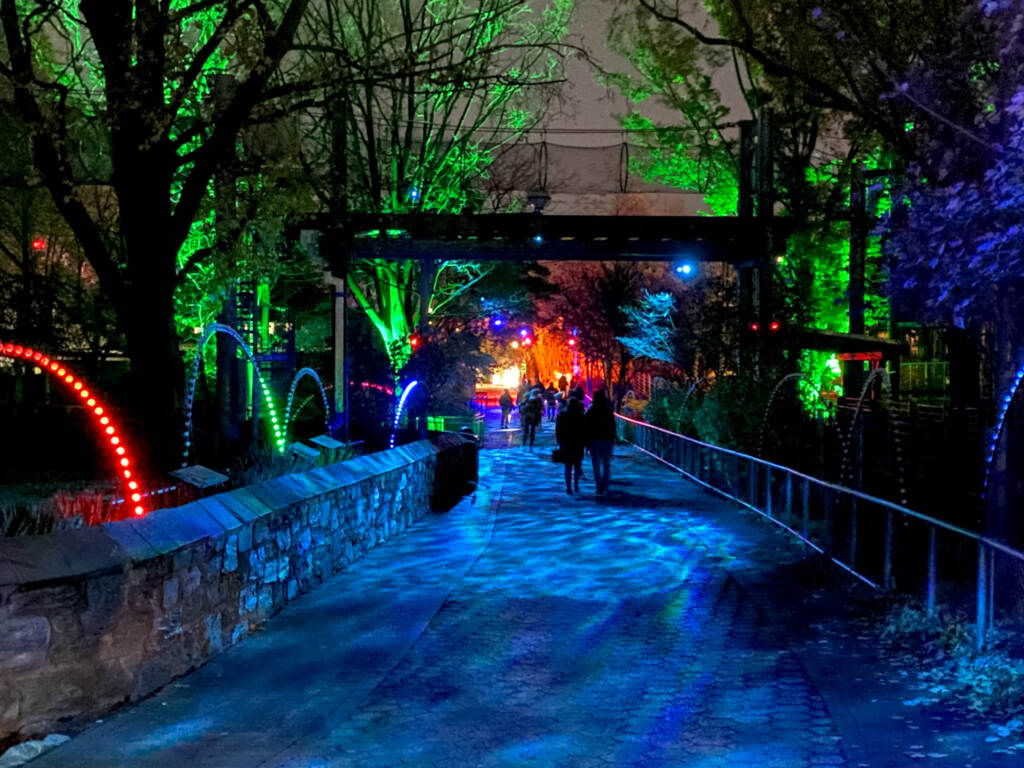 People walk through a lighted pathway at night.