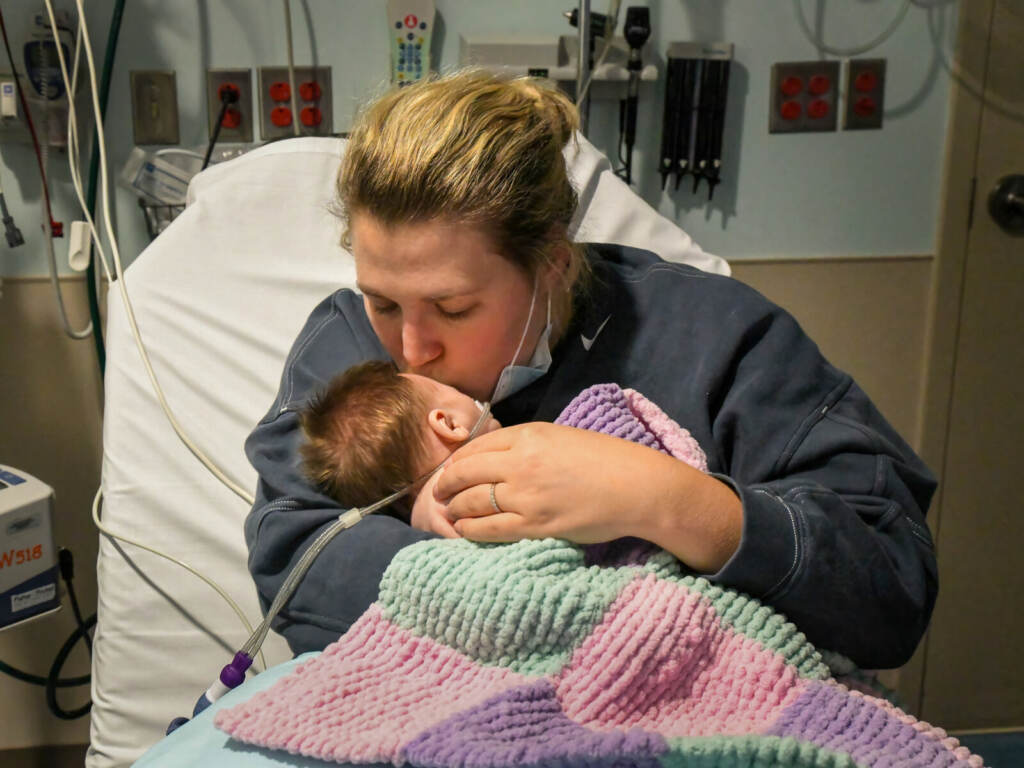 A woman holds a baby in her arms and kisses his head.