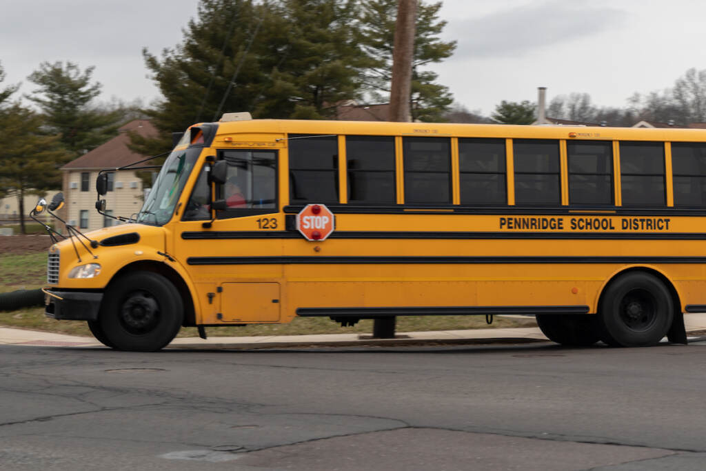 A school bus drives through Bucks County, Pa. (Kimberly Paynter/WHYY) A yellow school bus is driving on a road. The words on the side of the bus read