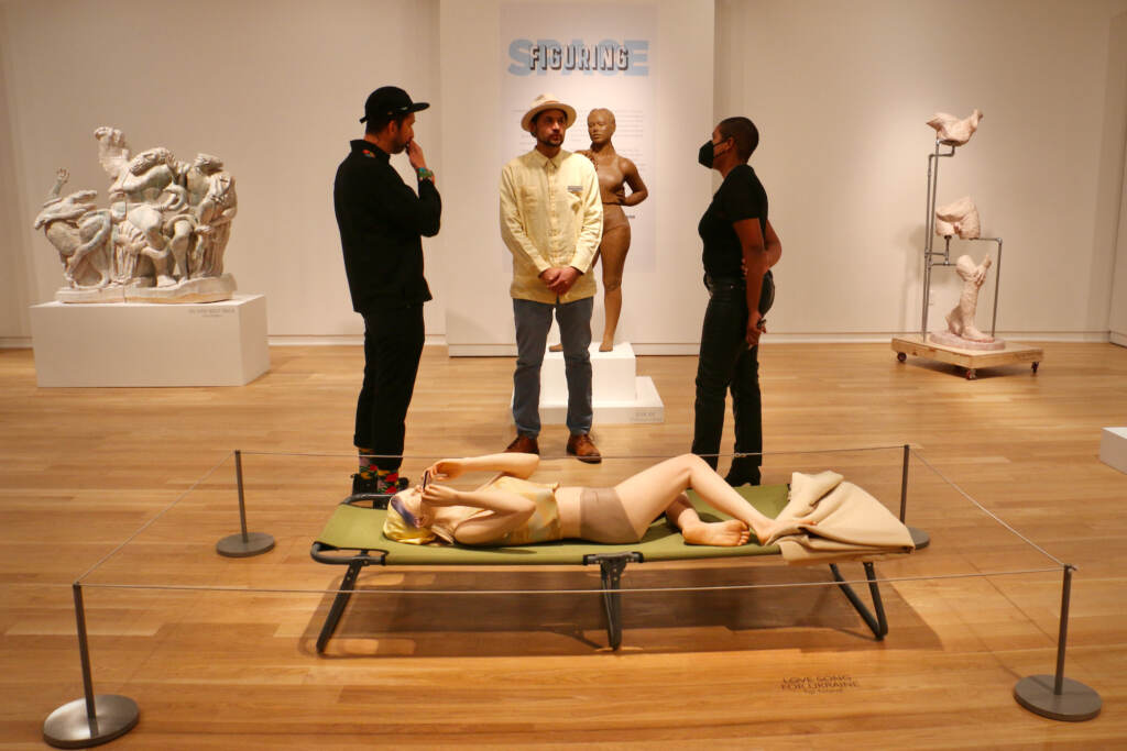Three artists stand in the middle of a gallery displaying sculptures.