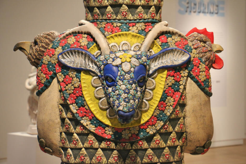 A close-up of a sculpted blue deer head on the back of a human figure sculpture.