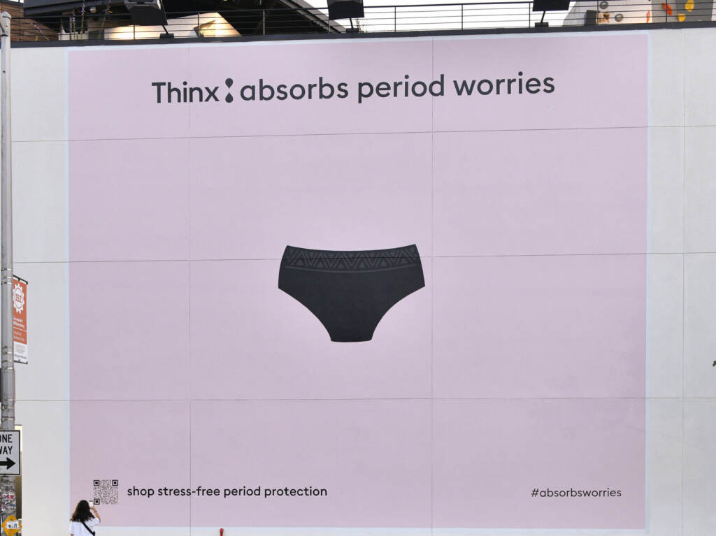 Thinx Unveils Interactive Billboard Experience In Brooklyn, NY To Launch “Thinx Absorbs Worries,” A Campaign Destigmatizing Good, Bad, Ugly And Funny Period Moments A photo of a large ad on a wall that has a light pink background and a picture of a pair of underwear along with the writing