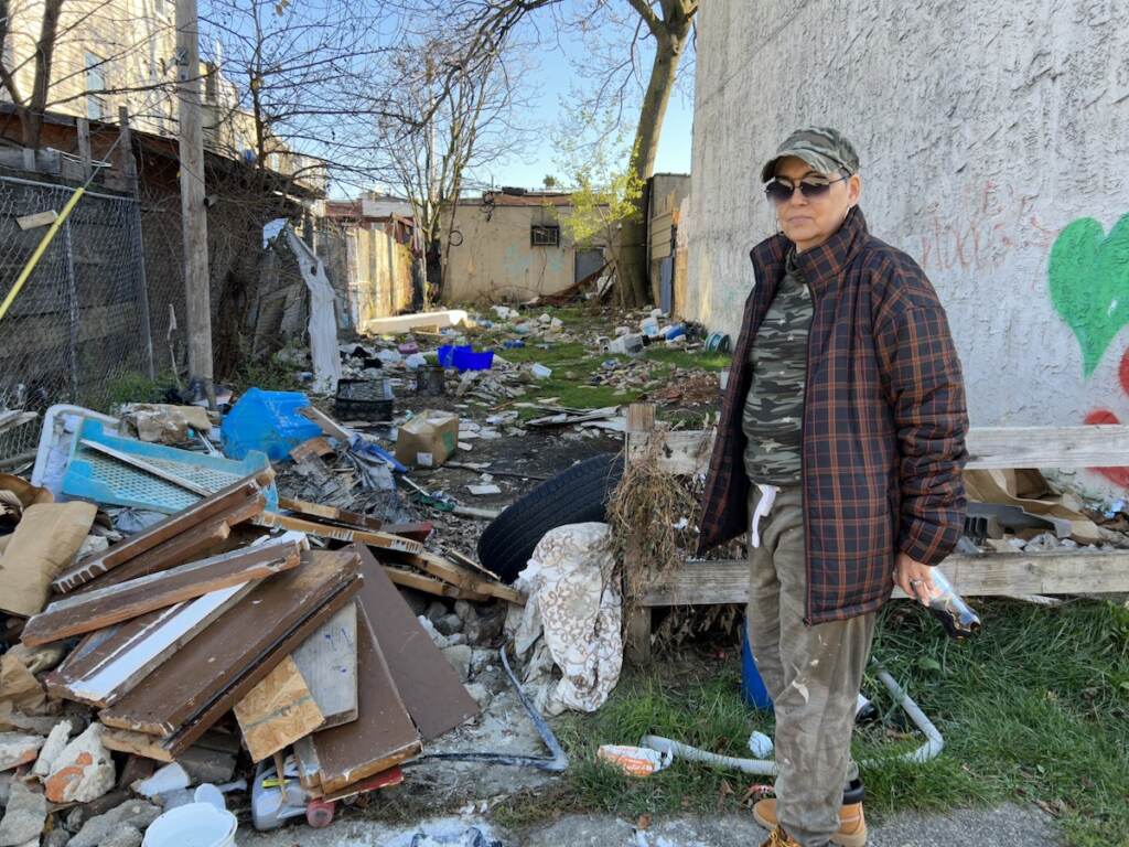 Marilyn Rodriguez stands in a vacant lot. A pile of debris is