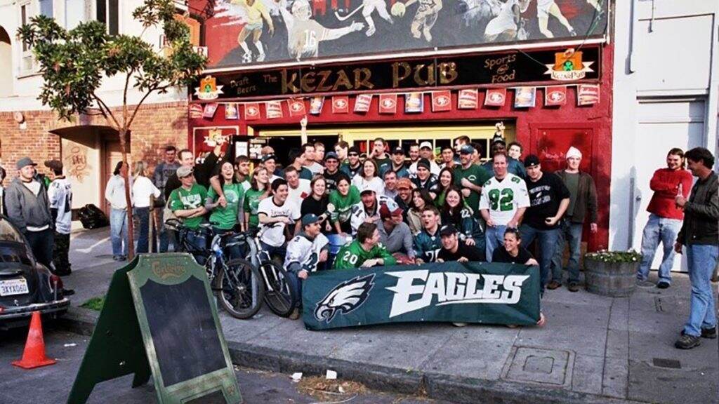 A group of people pose in front of a pub with a big Eagles banner.