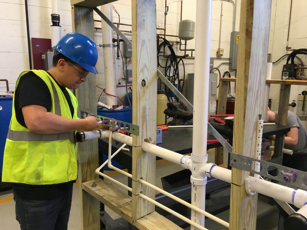 middle-bucks-institute-of-technology-plumbing-pipes-010223 A student in Middle Bucks Institute of Technology's HVAC/plumbing program uses a mock-up to practice installing a network of plumbing pipes