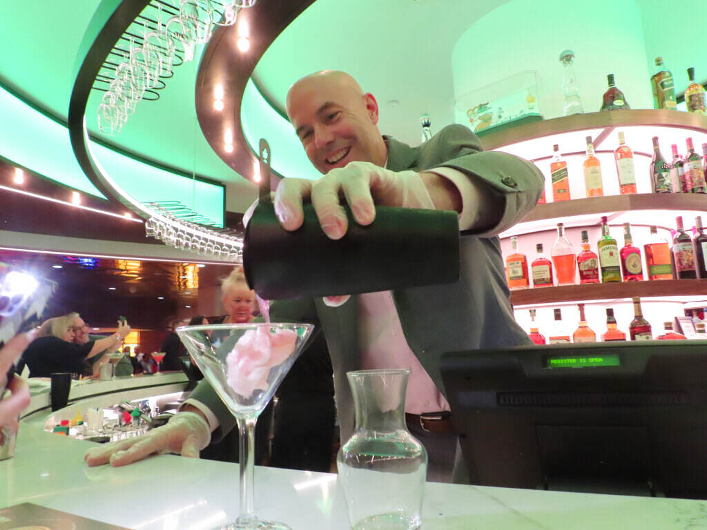A bartender pours a drink into a martini glass at a bar.