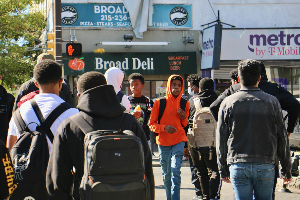 A crowd of people walk on the sidewalk.